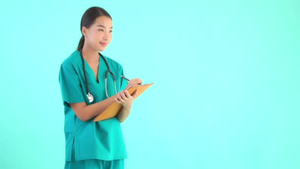 肖像画美しい若いアジアの医師の女性は青の隔離された背景にクリップボードで書く — ストック動画
