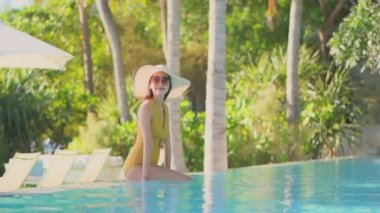Güzel Asyalı bir kadının, tatil için otel tatil beldesinde yüzme havuzunda dinlendiği görüntüler.