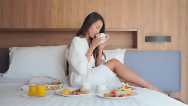 美丽的年轻亚洲女人喝咖啡和在床上吃早餐的镜头 — 图库视频影像