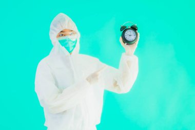Güzel bir portre genç Asyalı doktor. Özel süit ve maske takıyor. Mavi arka planda saati ya da alarmı gösteriyor.