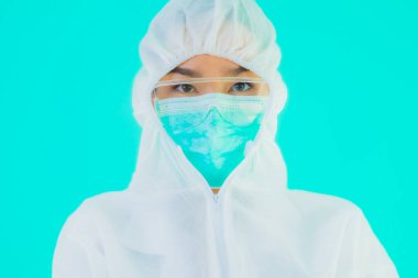 Güzel, genç Asyalı doktor kadın koronavirüsten korunmak için ppe ya da kişisel koruyucu ekipman takıyor ya da mavi izole arka planda beyaz kartı olan 19. bölgede yaşıyor.