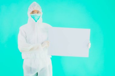 Güzel, genç Asyalı doktor kadın koronavirüsten korunmak için ppe ya da kişisel koruyucu ekipman takıyor ya da mavi izole arka planda beyaz kartı olan 19. bölgede yaşıyor.