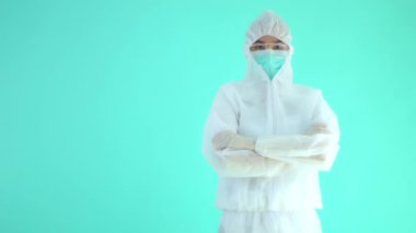 Korumalı tıbbi kıyafet giymiş ve kollarını çapraz bağlamış maskeli Asyalı bir kadının turkuazda izole edilmiş görüntüleri.
