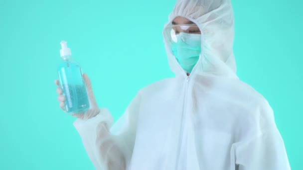 亚洲女人穿着防护服 戴着口罩 手里拿着一瓶绿松石隔离的清洁剂的镜头 — 图库视频影像