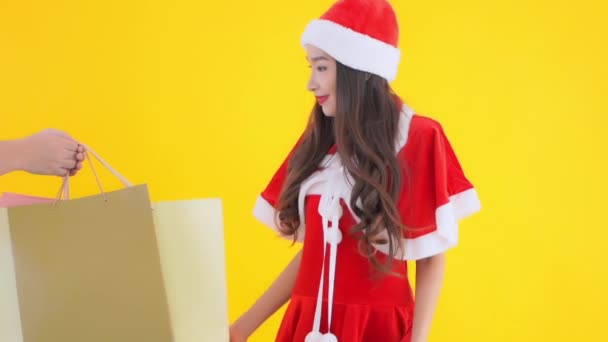 サンタスーツ姿の美しいアジア系女性の映像と黄色に隔離されたカラフルな紙袋 — ストック動画