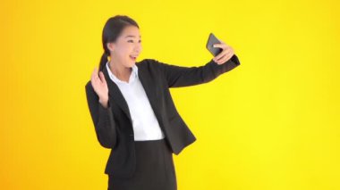 Asyalı güzel bir iş kadınının, sarı renkte izole edilmiş akıllı telefonuyla selfie çektiği görüntüler.