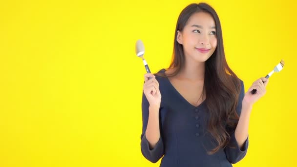 美丽的亚洲女人拿着用黄色隔离的勺子和叉子的镜头 — 图库视频影像
