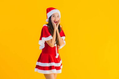 Güzel genç Asyalı kadın portresi Noel kıyafetleri ve şapka gülümsemesi sarı izole arka plandaki diğer hareketlerle mutlu.