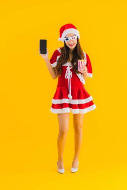 Güzel bir Asyalı kadın portresi patlamış mısır ve 3D gözlüklü noel şapkası takıyor sarı izole edilmiş arka planda film izlemeye hazır.