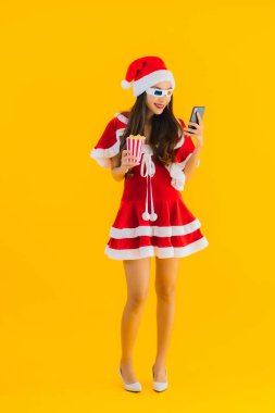 Güzel bir Asyalı kadın portresi patlamış mısır ve 3D gözlüklü noel şapkası takıyor sarı izole edilmiş arka planda film izlemeye hazır.