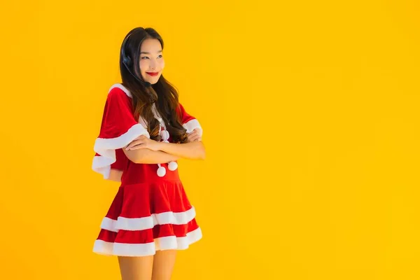 肖像画の美しい若いアジアの女性は 黄色の隔離された背景にコールセンターのためのヘッドフォンやヘッドセットとクリスマス服や帽子を着用 — ストック写真