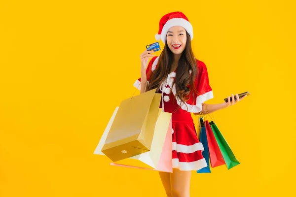 肖像画美しい若いアジアの女性は 黄色の隔離された背景に買い物袋の多くとクリスマス服の帽子を着用 — ストック写真