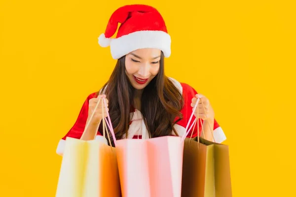 肖像画美しい若いアジアの女性は 黄色の隔離された背景に買い物袋の多くとクリスマス服の帽子を着用 — ストック写真