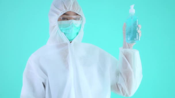 亚洲女人穿着防护服 戴着口罩 手里拿着一瓶绿松石隔离的清洁剂的镜头 — 图库视频影像