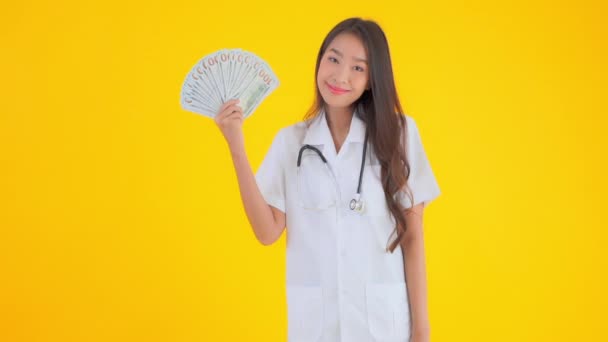 美丽的亚洲医生女人拿着一堆用黄色隔离的现金的镜头 — 图库视频影像