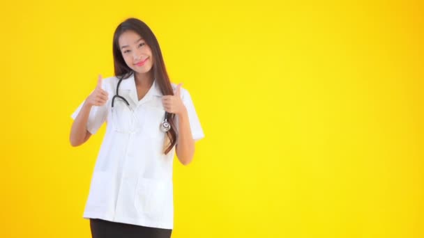 Metraje Hermosa Asiática Médico Mujer Mostrando Pulgares Arriba Aislado Amarillo — Vídeos de Stock
