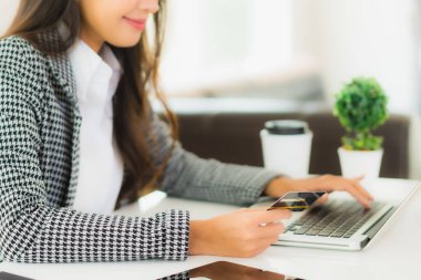 Güzel bir Asyalı kadının portresi online alışveriş malzemesi olarak dizüstü bilgisayarla kredi kartı kullanıyor.