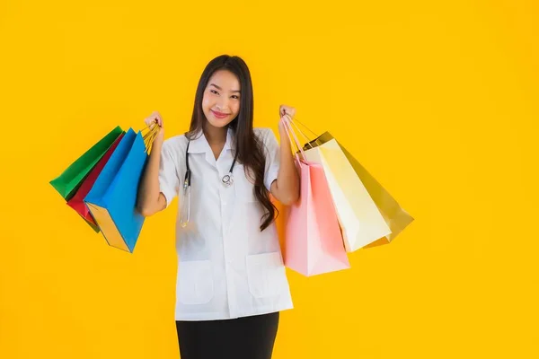 黄色の隔離された背景にショッピングモールやデパートからカラフルなショッピングバッグと肖像画の美しい若いアジアの医師の女性 — ストック写真