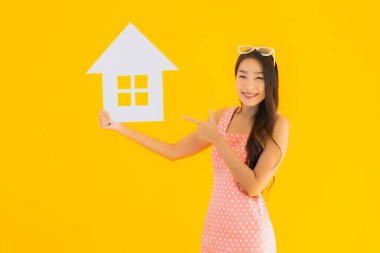 Güzel genç Asyalı kadın sarı izole arka planda ev ya da ev tabelasını gösteriyor.