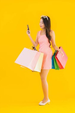 Renkli alışveriş çantalı güzel Asyalı kadın akıllı cep telefonu ve sarı izole edilmiş arka planda kredi kartı.
