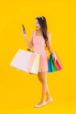 Renkli alışveriş çantalı güzel Asyalı kadın akıllı cep telefonu ve sarı izole edilmiş arka planda kredi kartı.
