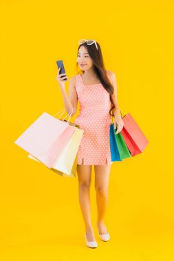 Renkli alışveriş çantalı güzel Asyalı kadın akıllı cep telefonu ve sarı izole edilmiş arka planda kredi kartı.