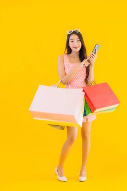 Renkli alışveriş çantalı güzel Asyalı kadın akıllı cep telefonu ve sarı izole edilmiş arka planda kredi kartı.