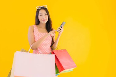 Renkli alışveriş çantalı güzel Asyalı kadın akıllı cep telefonu ve sarı izole edilmiş arka planda kredi kartı.