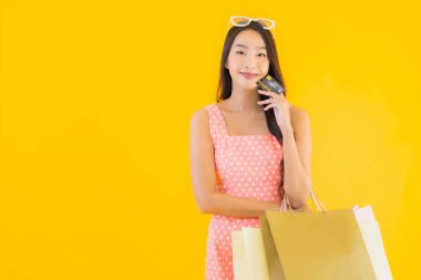Renkli alışveriş çantalı güzel Asyalı kadın akıllı cep telefonu ve sarı izole edilmiş arka planda kredi kartı.