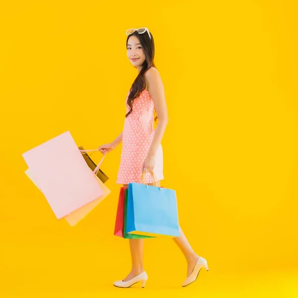 デパートのカラフルなショッピングバッグと黄色の隔離された背景にショッピングモールと肖像画の美しい若いアジアの女性 — ストック写真