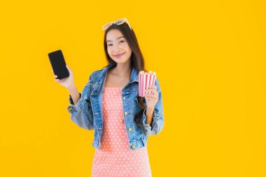 Güzel bir Asyalı kadın portresi telefon patlamış mısırı ve sarı izole edilmiş bir arka planda film izlemekten memnun.