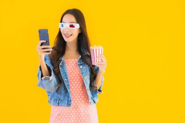 Güzel bir Asyalı kadın portresi telefon patlamış mısırı ve sarı izole edilmiş bir arka planda film izlemekten memnun.