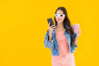 Güzel bir Asyalı kadın portresi telefon patlamış mısırı ve sarı izole edilmiş bir arka planda film izlemekten memnun.