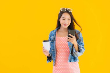 Kahve fincanı ve sarı izole edilmiş arka planda akıllı cep telefonlu güzel Asyalı kadın portresi.