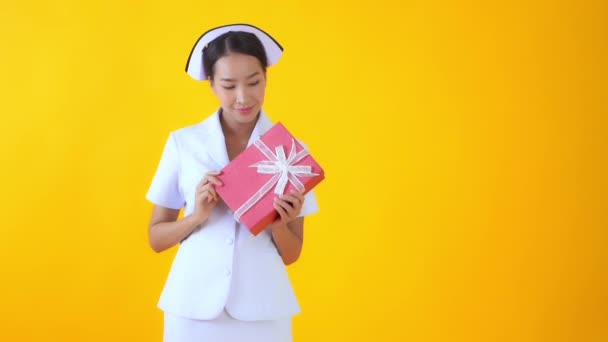黄色に隔離された赤いギフトボックスを持つ美しいアジアの看護師の映像 — ストック動画
