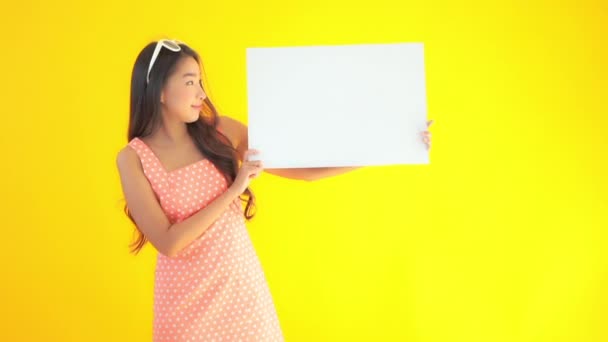 Кадри Красивої Азіатської Жінки Тримає Порожню Білу Дошку Ізольовано Жовтому — стокове відео