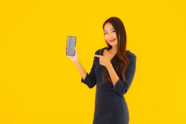 Akıllı cep telefonlu güzel Asyalı kadın portresi ya da sarı izole edilmiş arka planda cep telefonu.