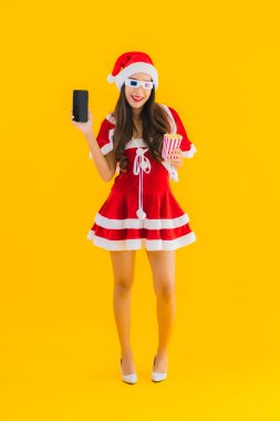 Güzel bir Asyalı kadın portresi patlamış mısır ve 3D gözlüklü noel şapkası takıyor sarı izole edilmiş arka planda film izlemeye hazır.