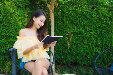 Genç Asyalı kadın bahçe manzarası hakkında kitap okuyor.