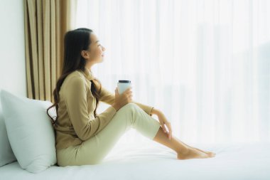 Yatak odasının iç tarafında, kahve fincanı olan Asyalı genç bir kadın.