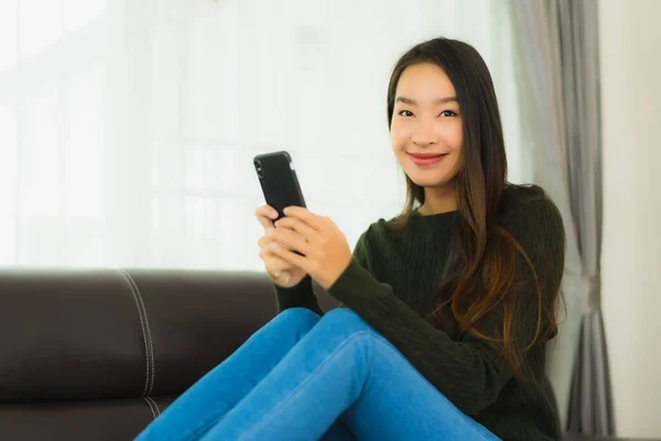 漂亮的年轻亚洲女人在客厅的沙发上使用智能手机或手机 — 图库照片