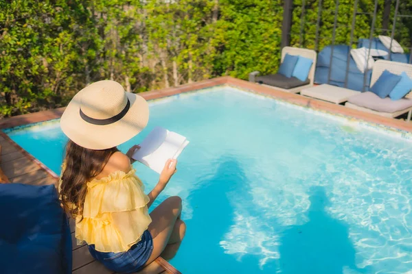 Portrait young asian woman read book around outdoor swimming pool in hotel resort