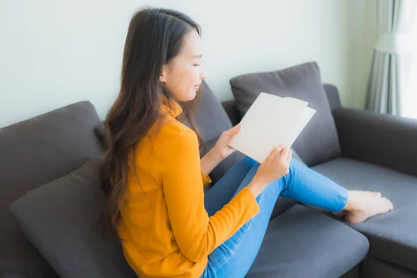 画像年轻的亚洲女人在客厅的沙发上看书 沙发上有枕头 — 图库照片