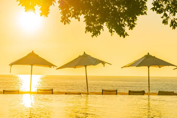 日没や旅行休暇のための日の出時に屋外スイミングプールの周りに傘と椅子と美しい熱帯屋外ビーチの海の海 — ストック写真