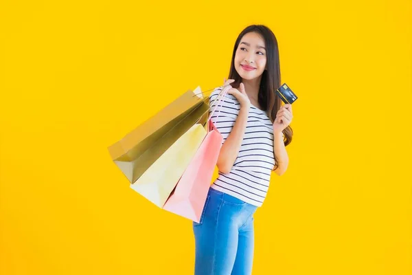 色彩艳丽的年轻亚洲女人 背负着五颜六色的购物袋和黄色独立背景的信用卡 — 图库照片