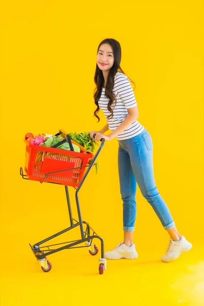 노란색외진 배경에 슈퍼마켓 카트에서 식료품을 아름다운 아시아 여자의 — 스톡 사진