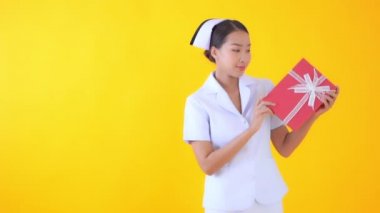 Sarıya izole edilmiş kırmızı hediye kutusu taşıyan güzel Asyalı hemşire görüntüleri.