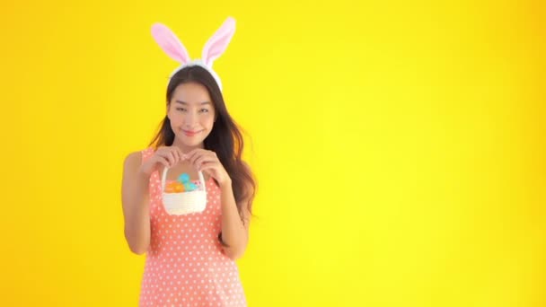 アジアの美しい女性の映像ウサギの耳と黄色に隔離されたニンジンとバスケット — ストック動画