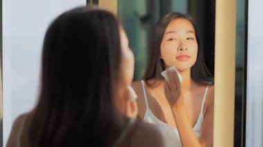 Güzel Asyalı bir kadının aynanın karşısında yüzünü sildiği görüntüler.