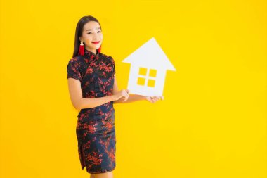 Güzel bir Asyalı kadın portresi, Çin elbisesi giyiyor. Sarı izole arka planda ev işareti var.